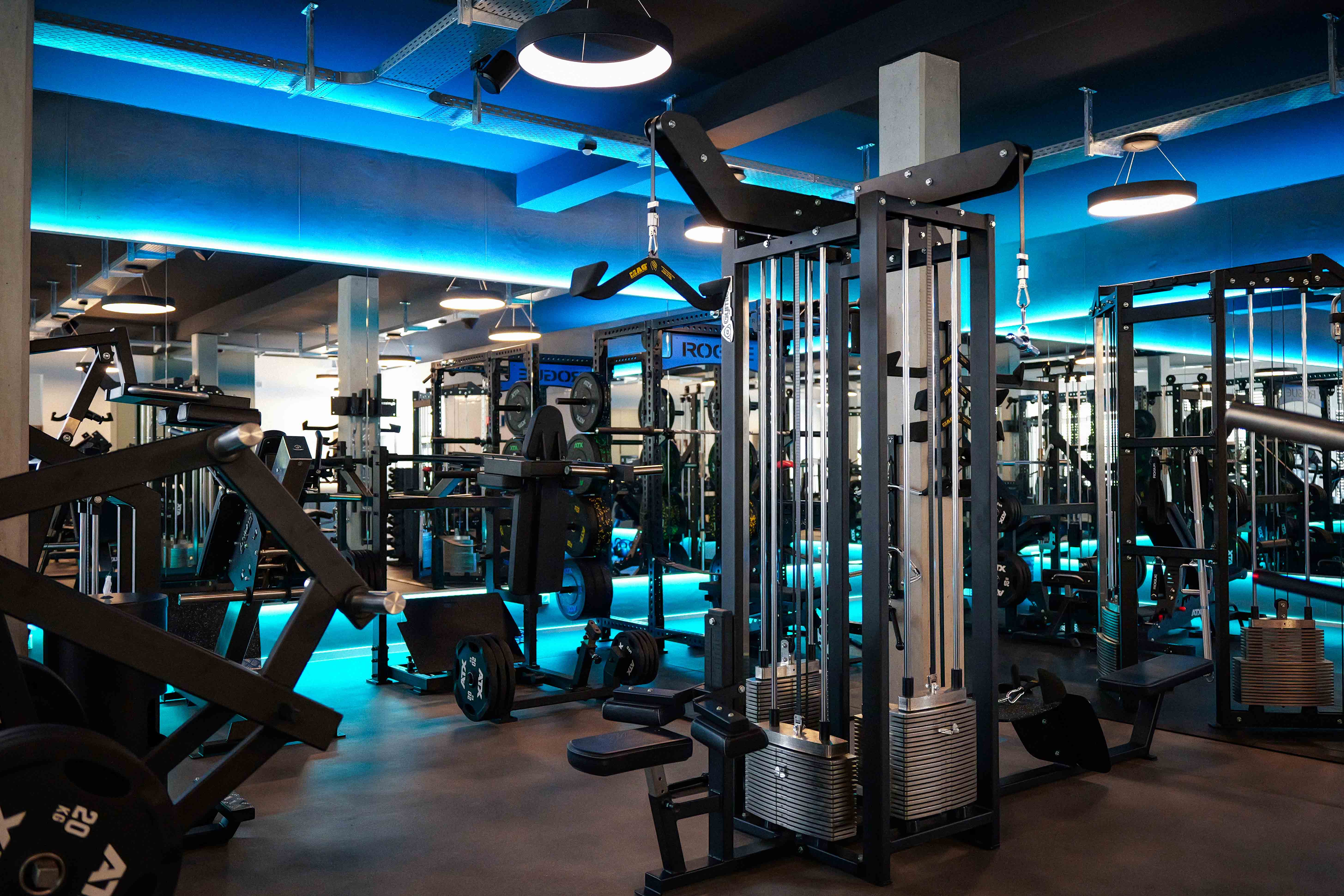 Moderne Fitnessstudio mit Krafttrainingsgeräten und blauweißer LED-Beleuchtung an Decke und Boden.