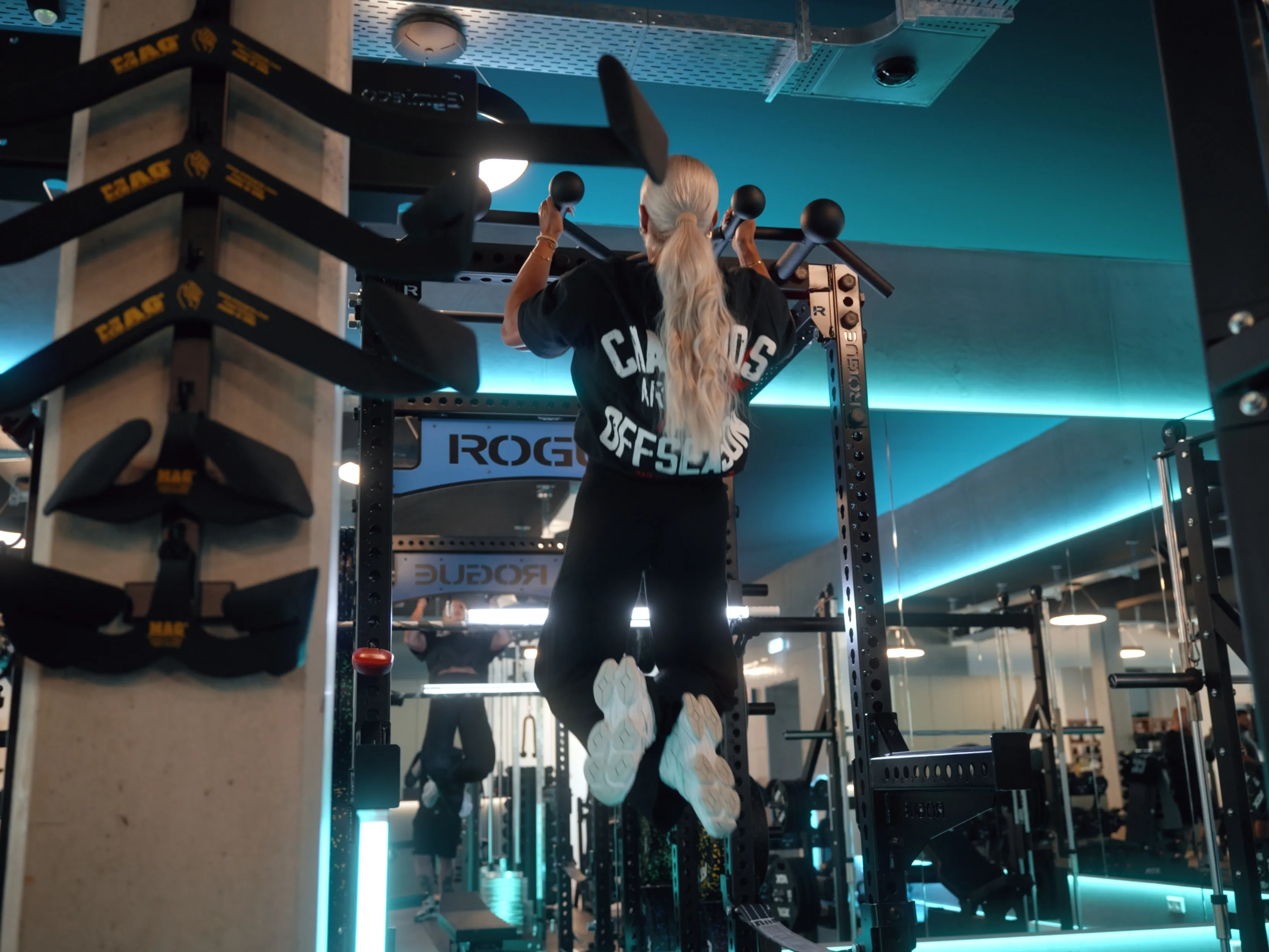 Frau macht Klimmzüge an einer Rogue-Pull-up-Stange in einem modernen Fitnessstudio.