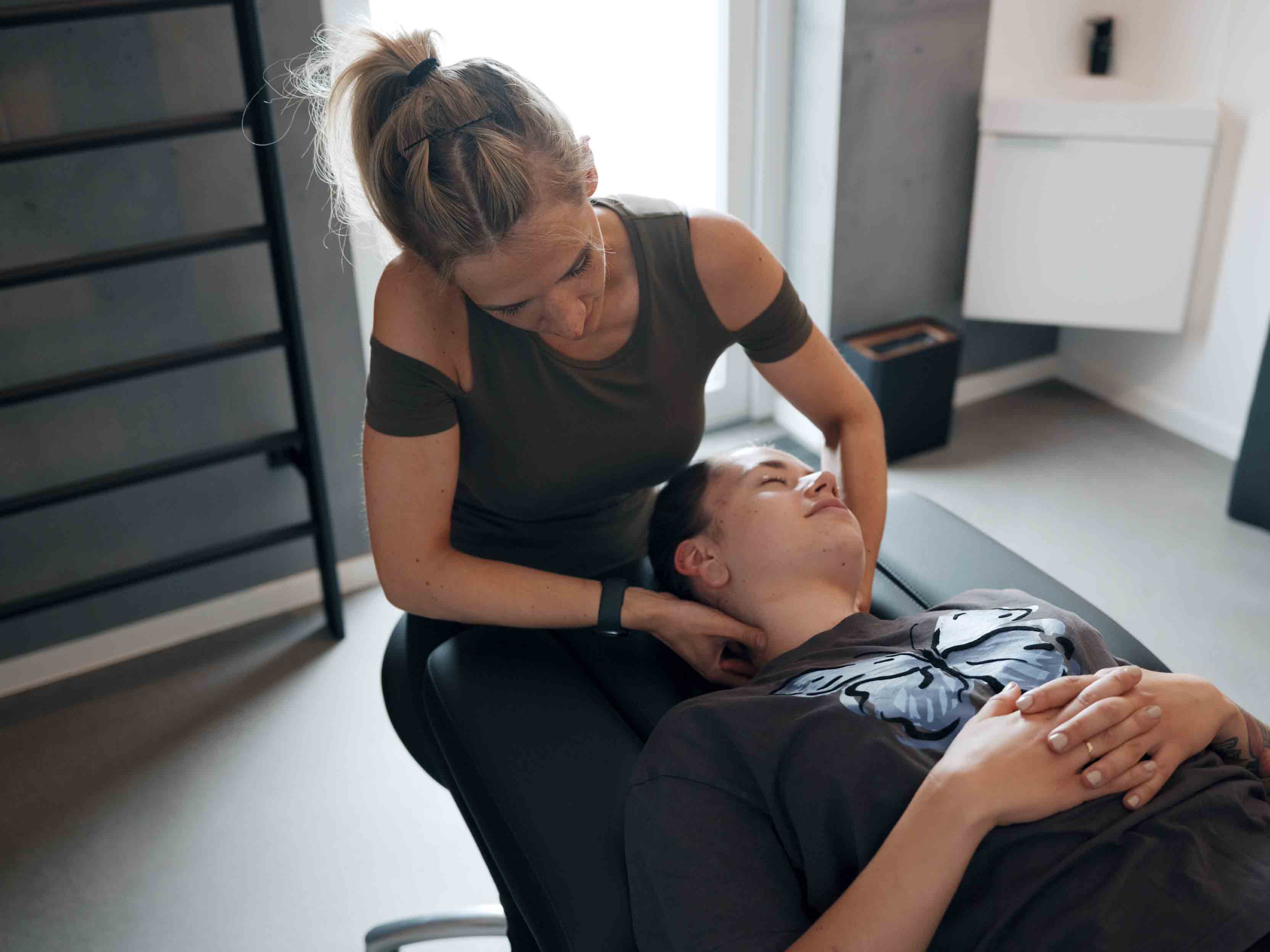 Frau behandelt entspannten Patienten, der auf einer Liege mit Schmetterlings-T-Shirt liegt.